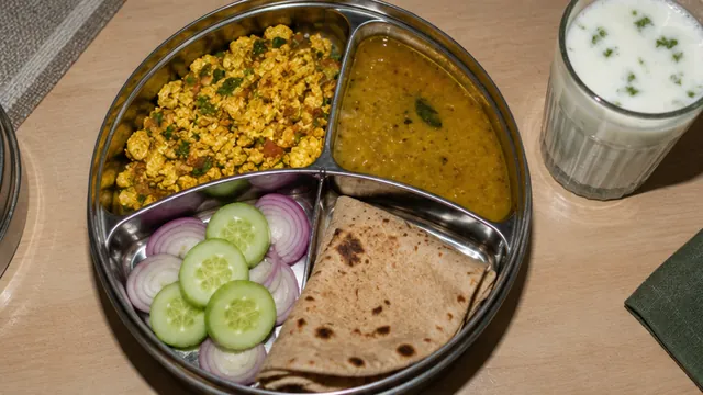 A round steel lunch box with paneer, dal, salad and roti